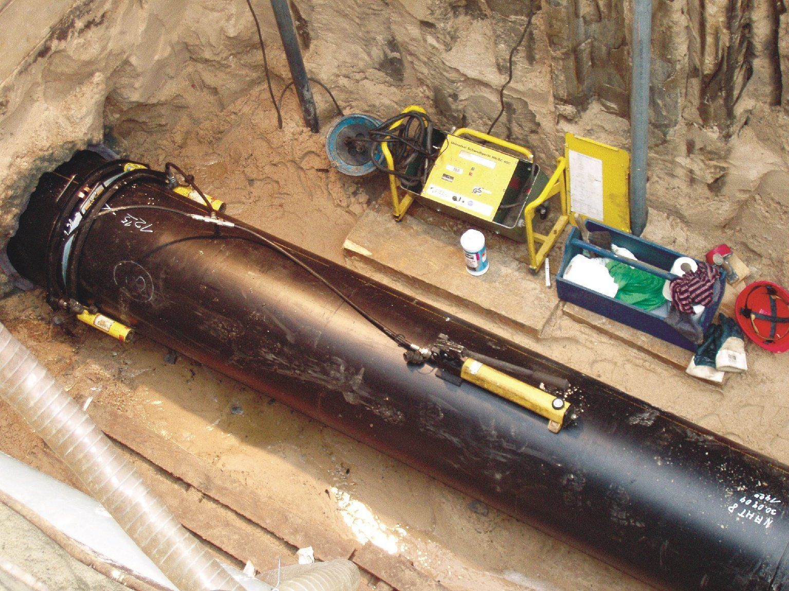 A large black pipe is laying in the dirt next to tools.