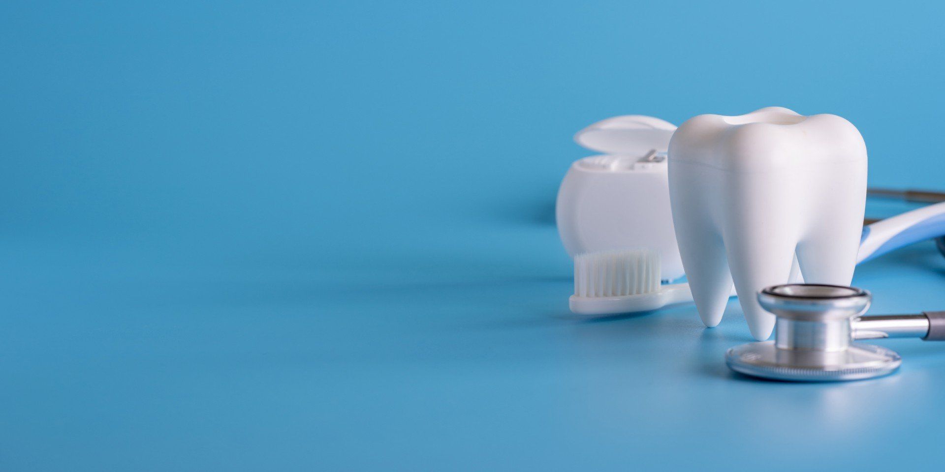A white tooth, dental floss, and a stethoscope on a blue background, representing dental health.