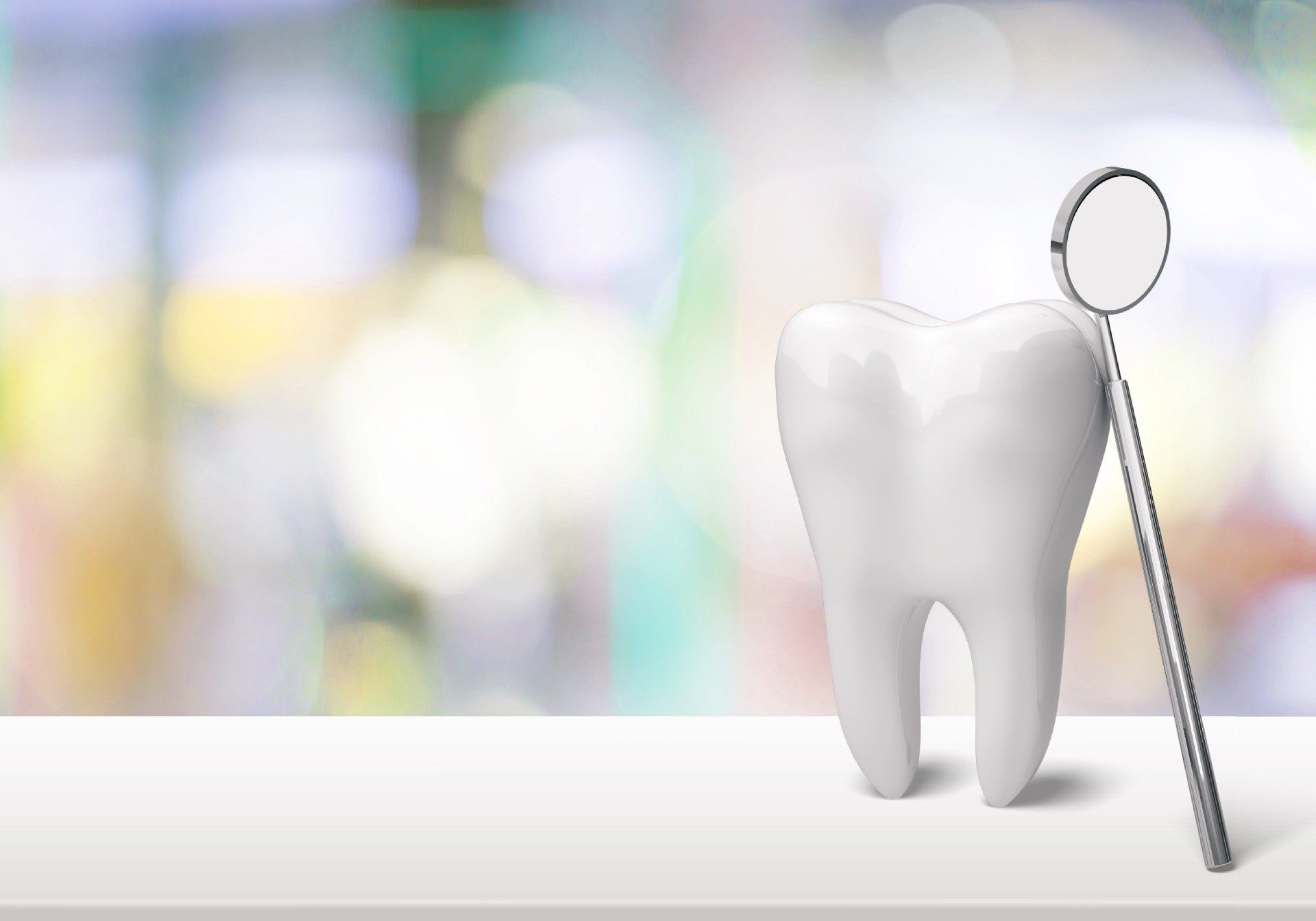 White tooth and dental mirror on a white surface with a blurred background, suggesting a dental setting.