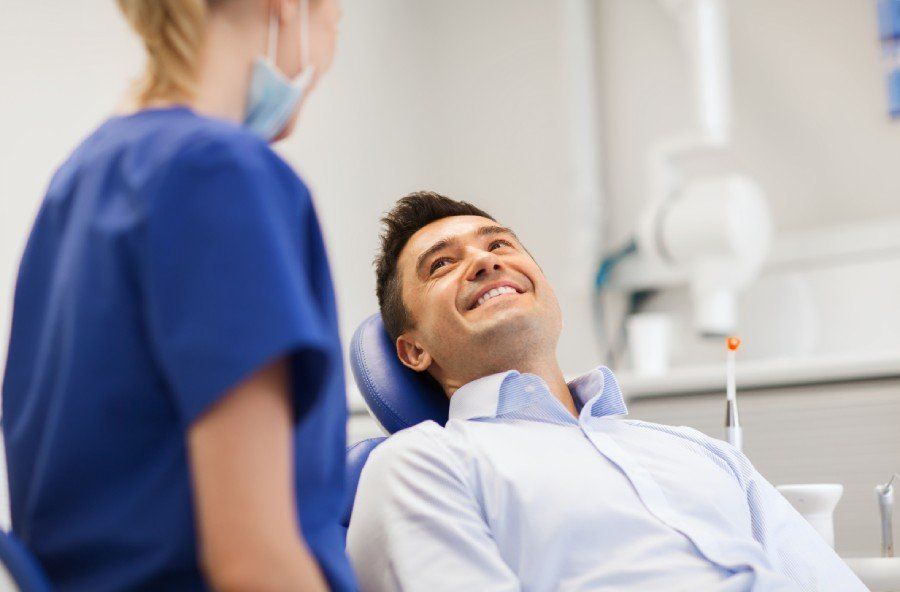 An implant procedure in progress in St. Peters, MO Man in dental chair smiles at dental assistant in clinic.
