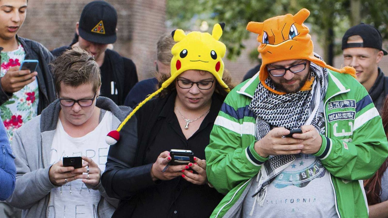A group of people wearing pikachu hats are looking at their phones.