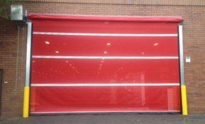 A red garage door is sitting on the side of a brick building.