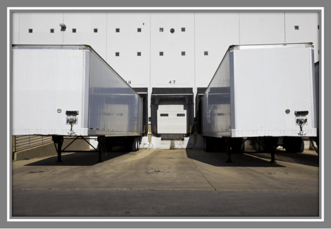 A row of semi trucks are docked at a warehouse