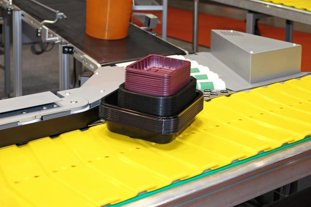 A conveyor belt with a stack of plastic containers on it.