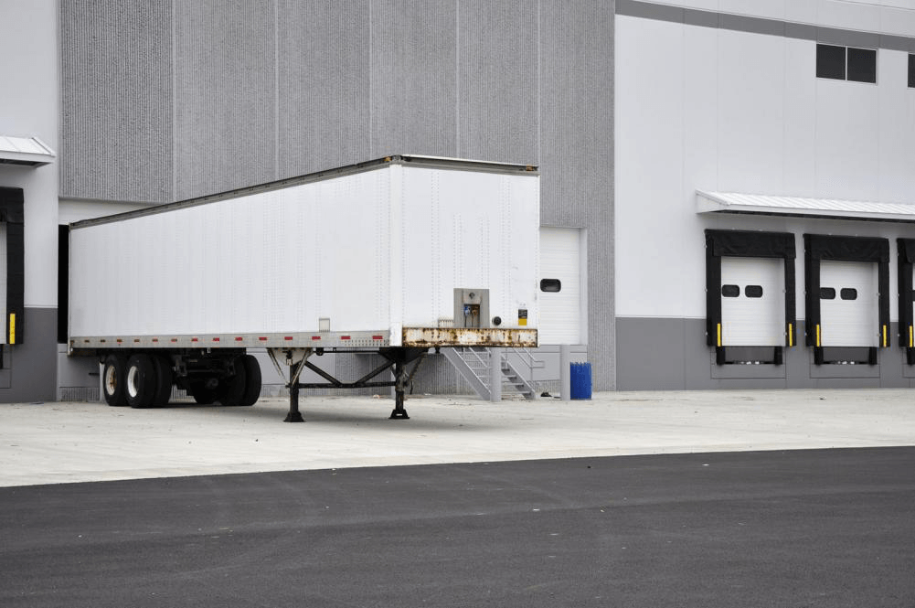 A semi truck is parked in front of a warehouse.
