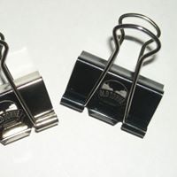Two binder clips are sitting on top of each other on a white surface.