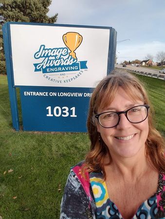 A woman wearing glasses is smiling in front of a sign for image awards engraving.