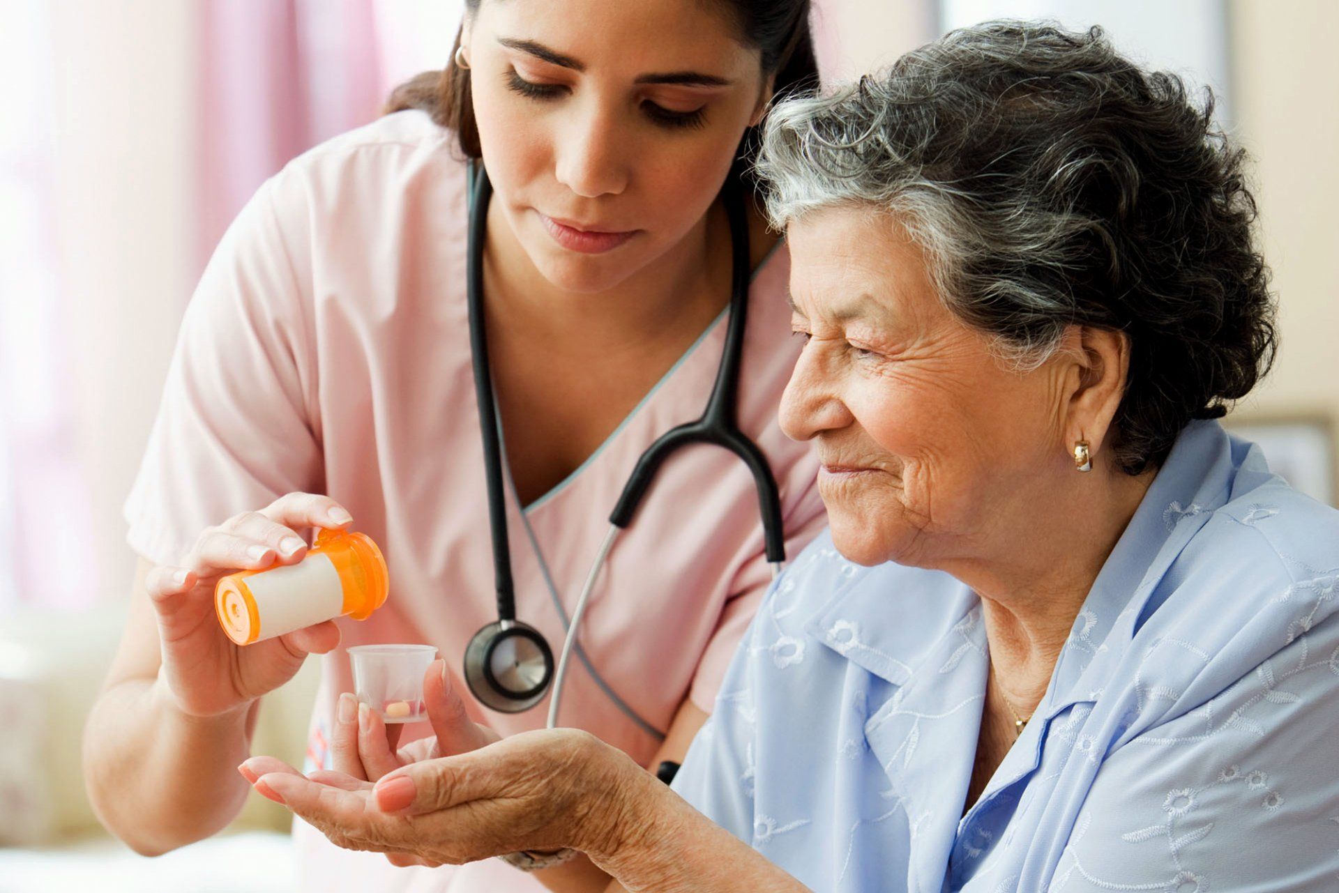 Female nures wearing pink scrubs giving medication to older woman