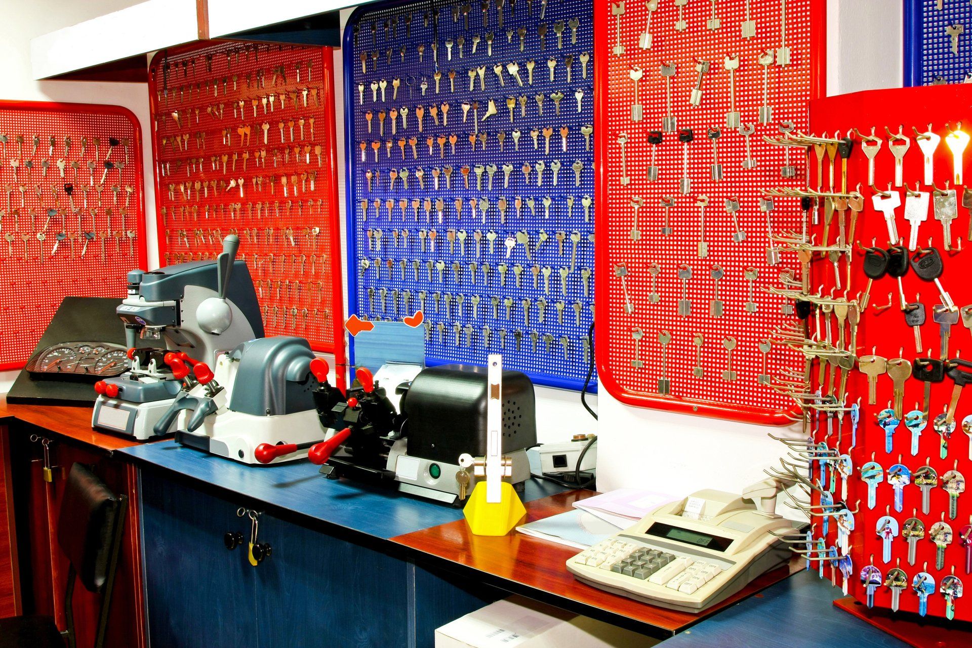 A locksmith shop interior; key cutting machines, key racks, and a telephone on a blue counter.