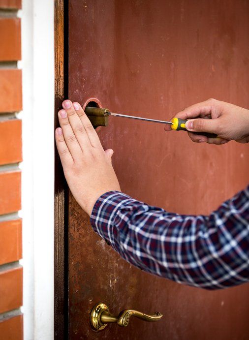 Person using a screwdriver to remove a lock from a brown door.