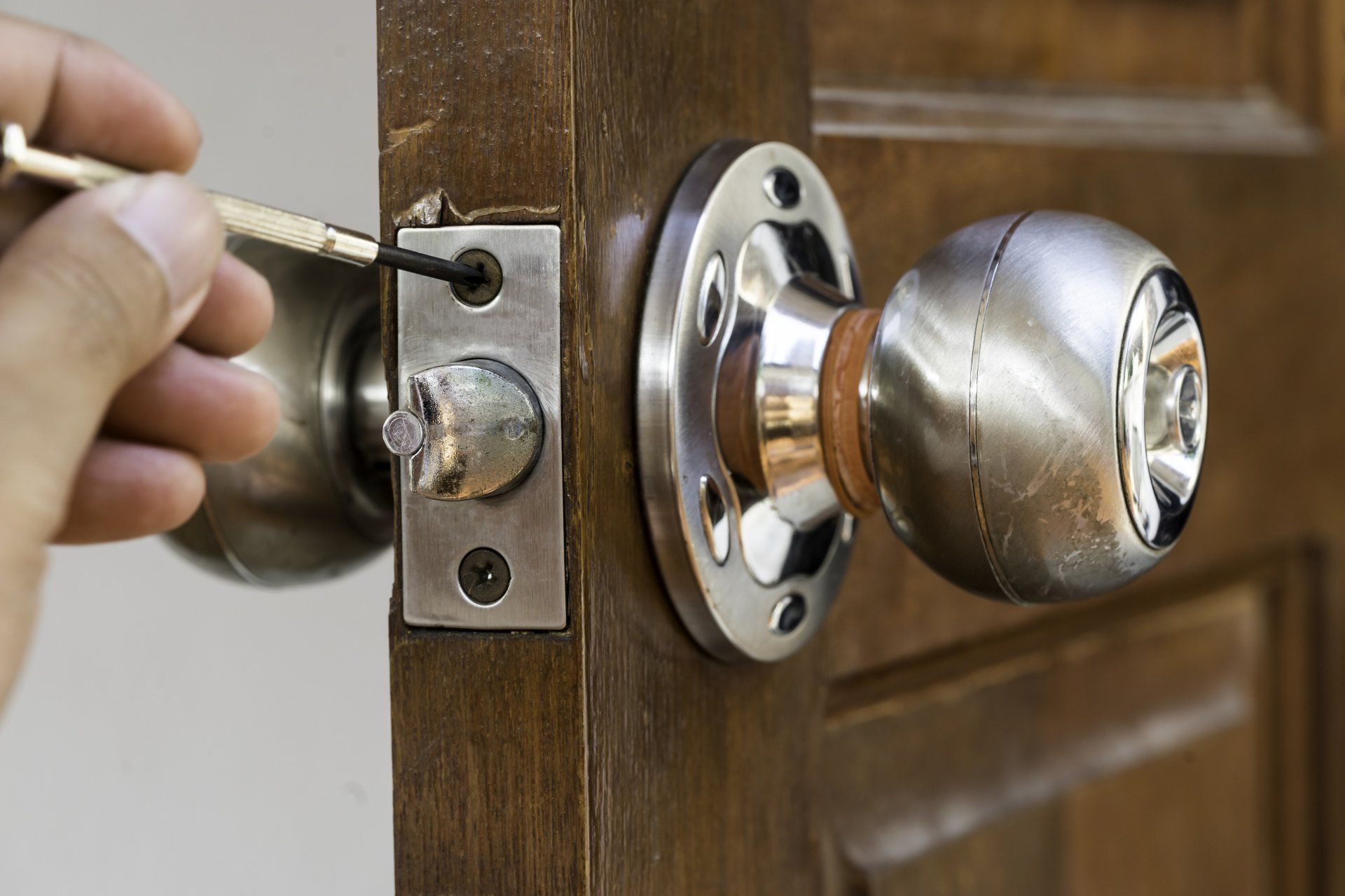 Person using a screwdriver to fix a door handle on a wooden door.