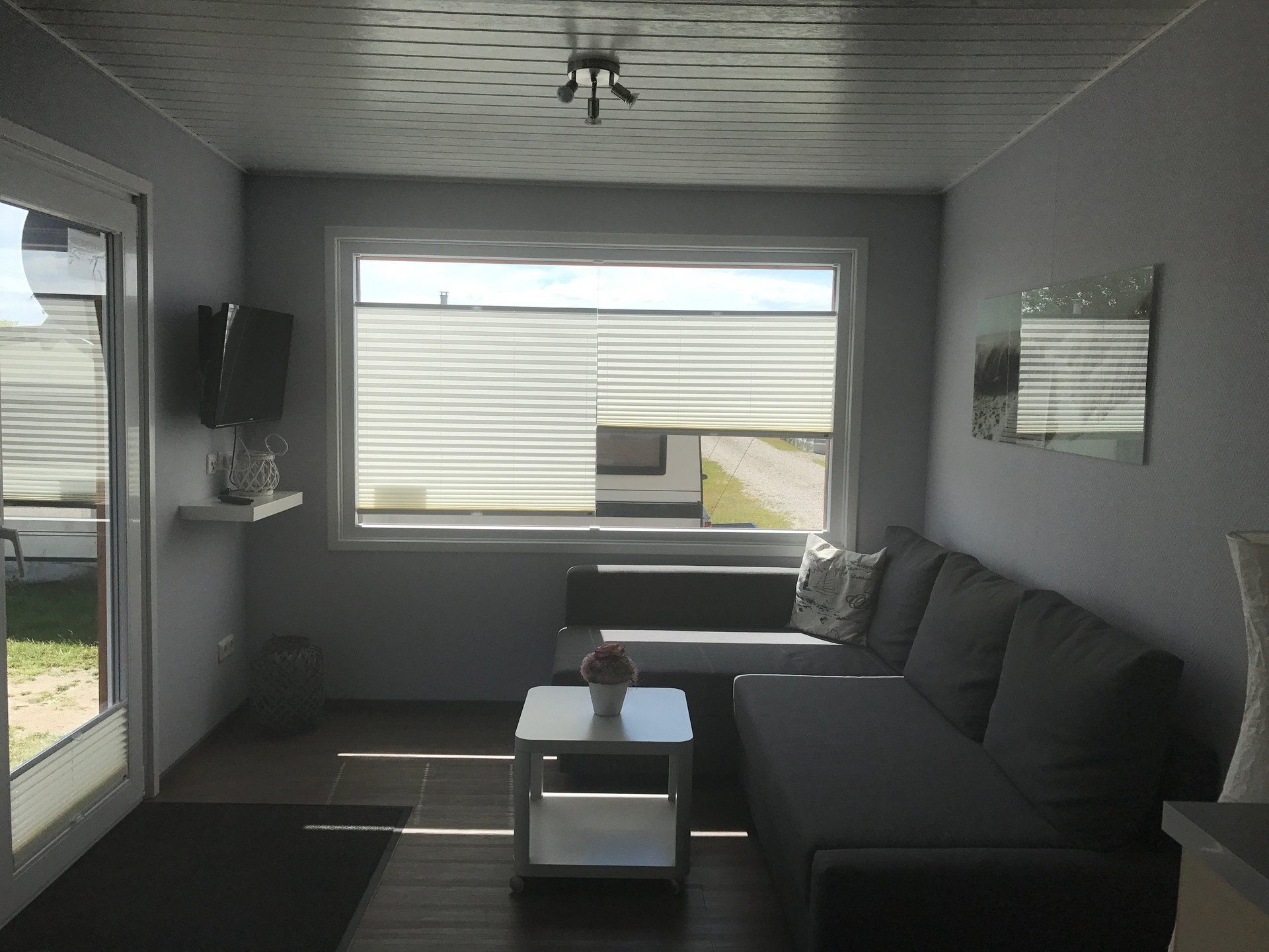 Wohnzimmer mit grauem Sofa, kleinem Tisch, Fenster mit Jalousie und Schiebetür.
