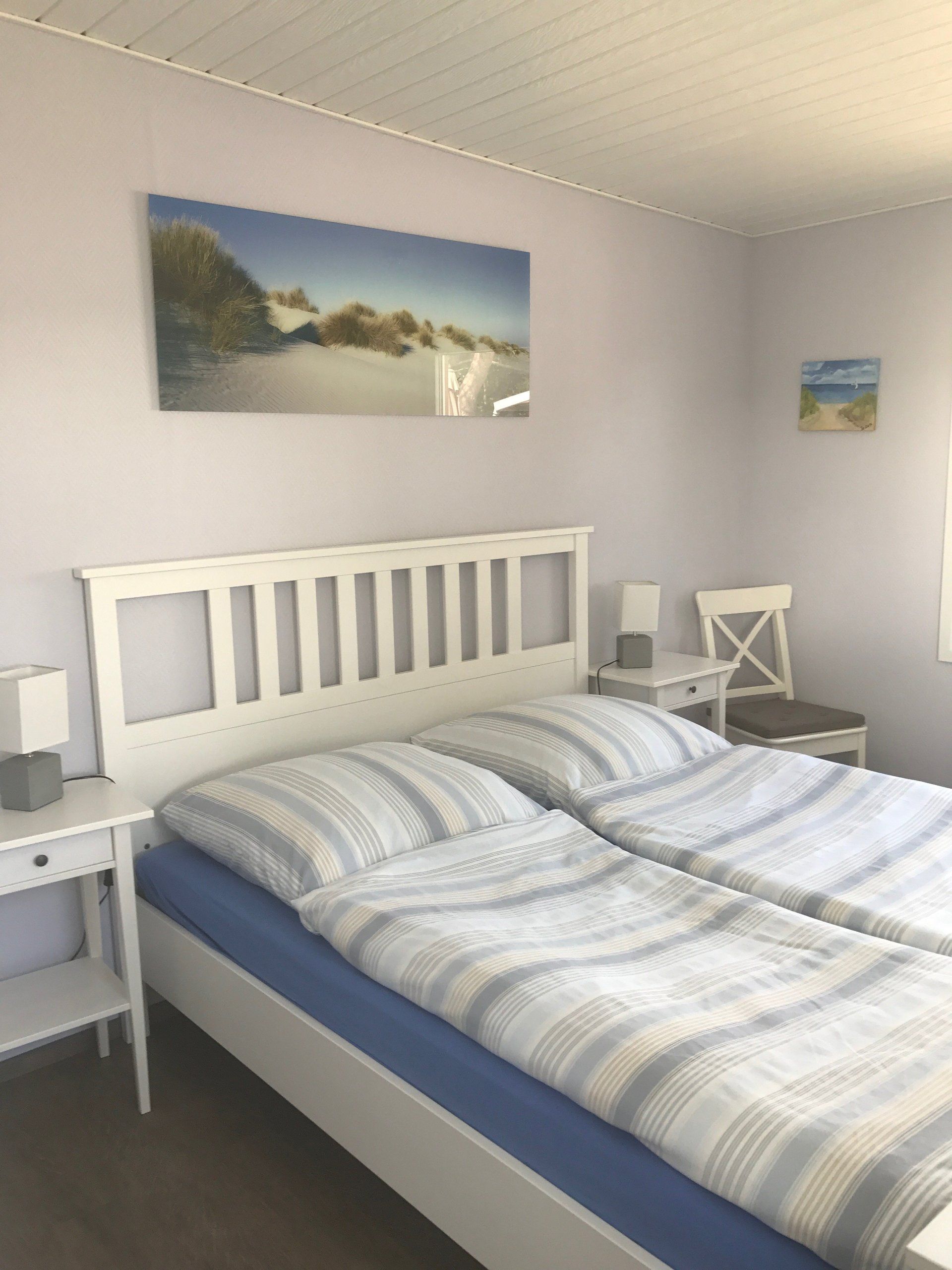 Schlafzimmer mit zwei Einzelbetten, weißem Kopfteil, blau-weiß gestreifter Bettwäsche, Kunstwerk einer Strandszene.