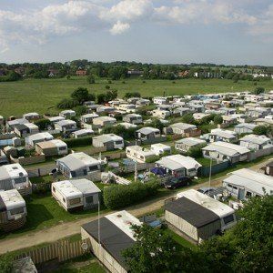 Draufsicht auf einen überfüllten Wohnwagenpark mit zahlreichen weißen und grauen Campern auf einer Wiese.
