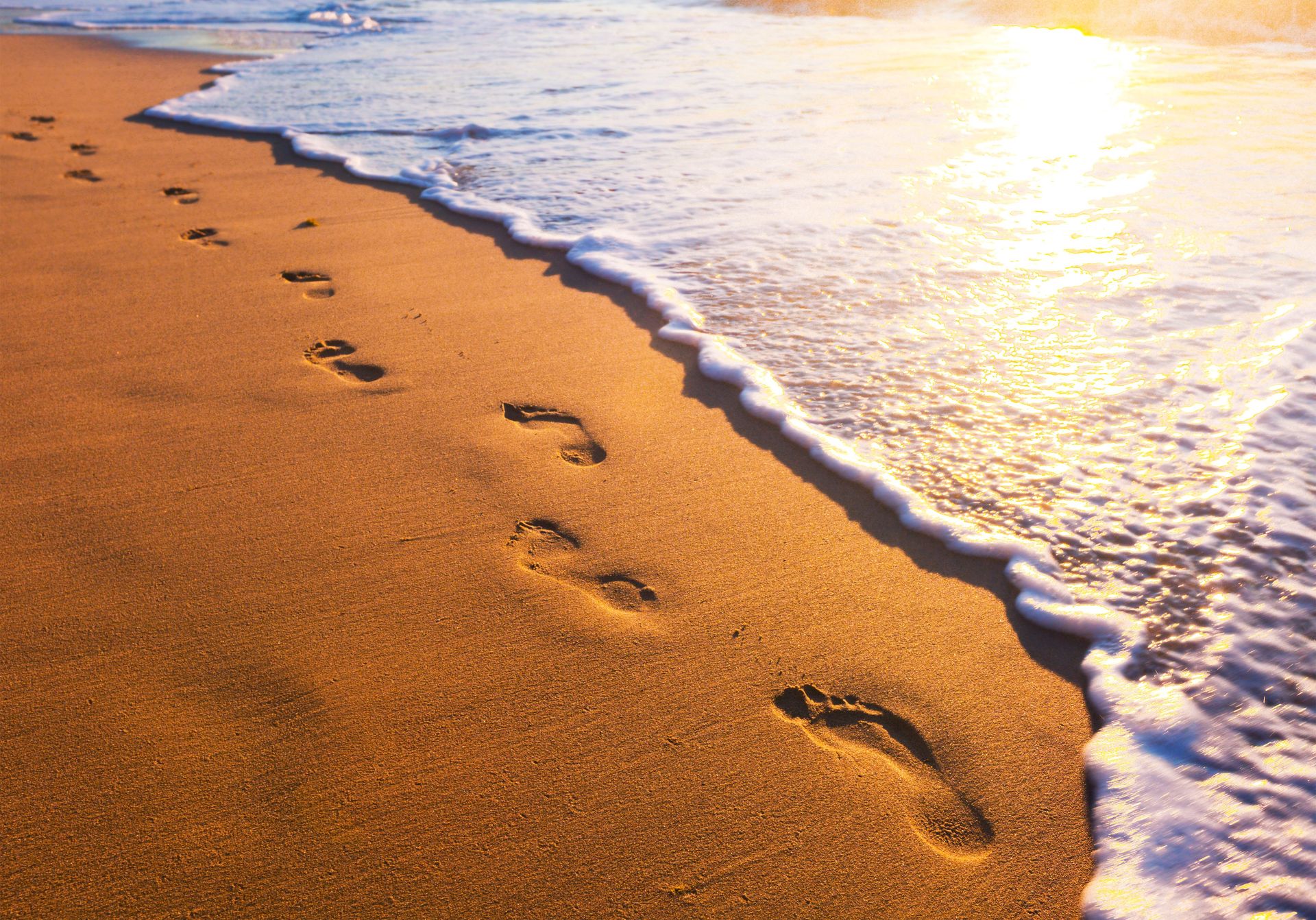 Fußabdrücke im Sand neben den Meereswellen während der goldenen Stunde.