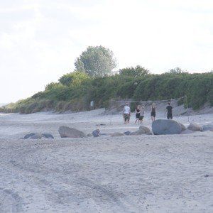 Strandszene mit einem Volleyballnetz; Menschen spielen in der Nähe eines dünenbedeckten Hügels.