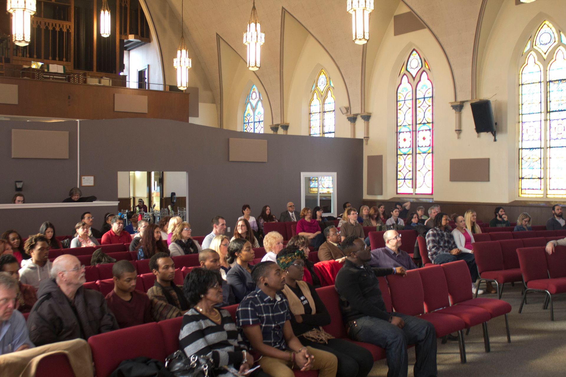 A large group of people are sitting in a church with stained glass windows.