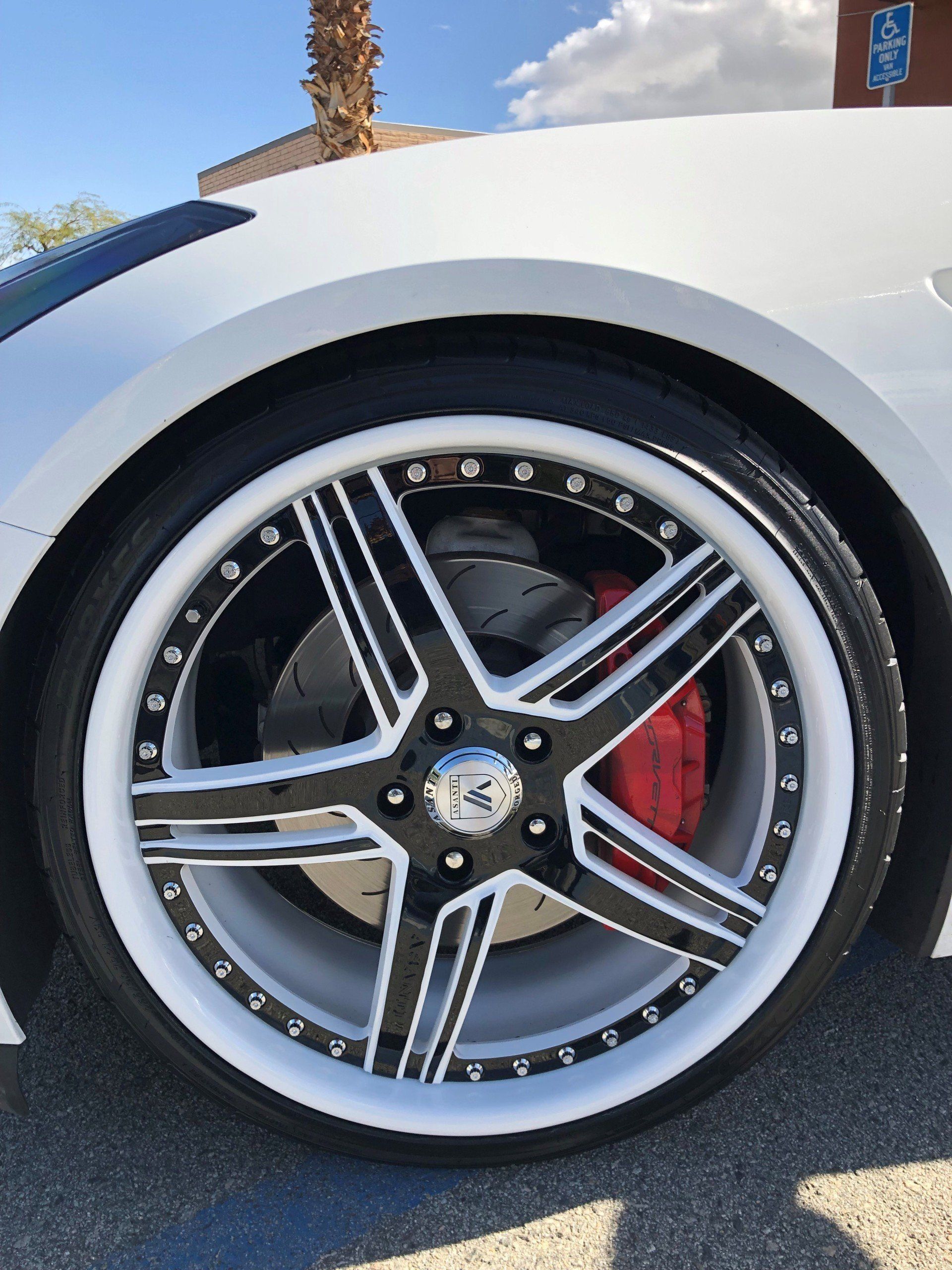 A white car with black and white wheels and red brake calipers
