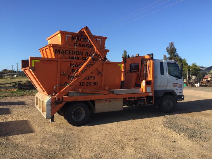 Macedon Ranges Mini Skips truck carrying a loaded orange skip bin