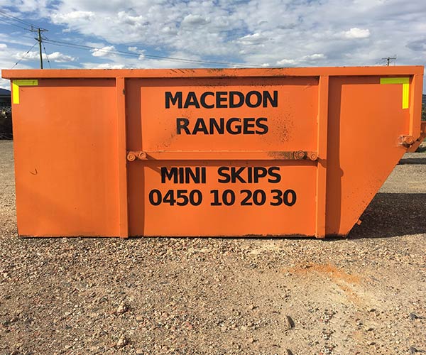 Orange Macedon Ranges Mini Skips skip bin on a gravel driveway