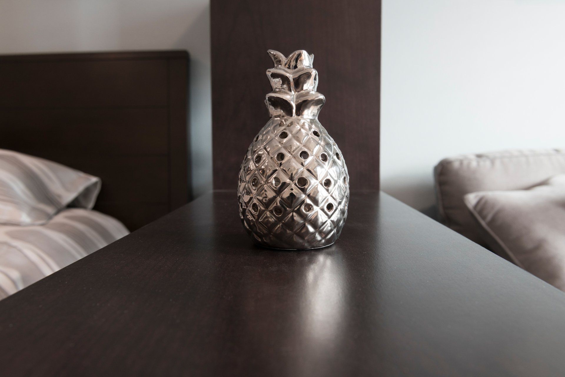 A silver pineapple is sitting on a nightstand next to a bed.