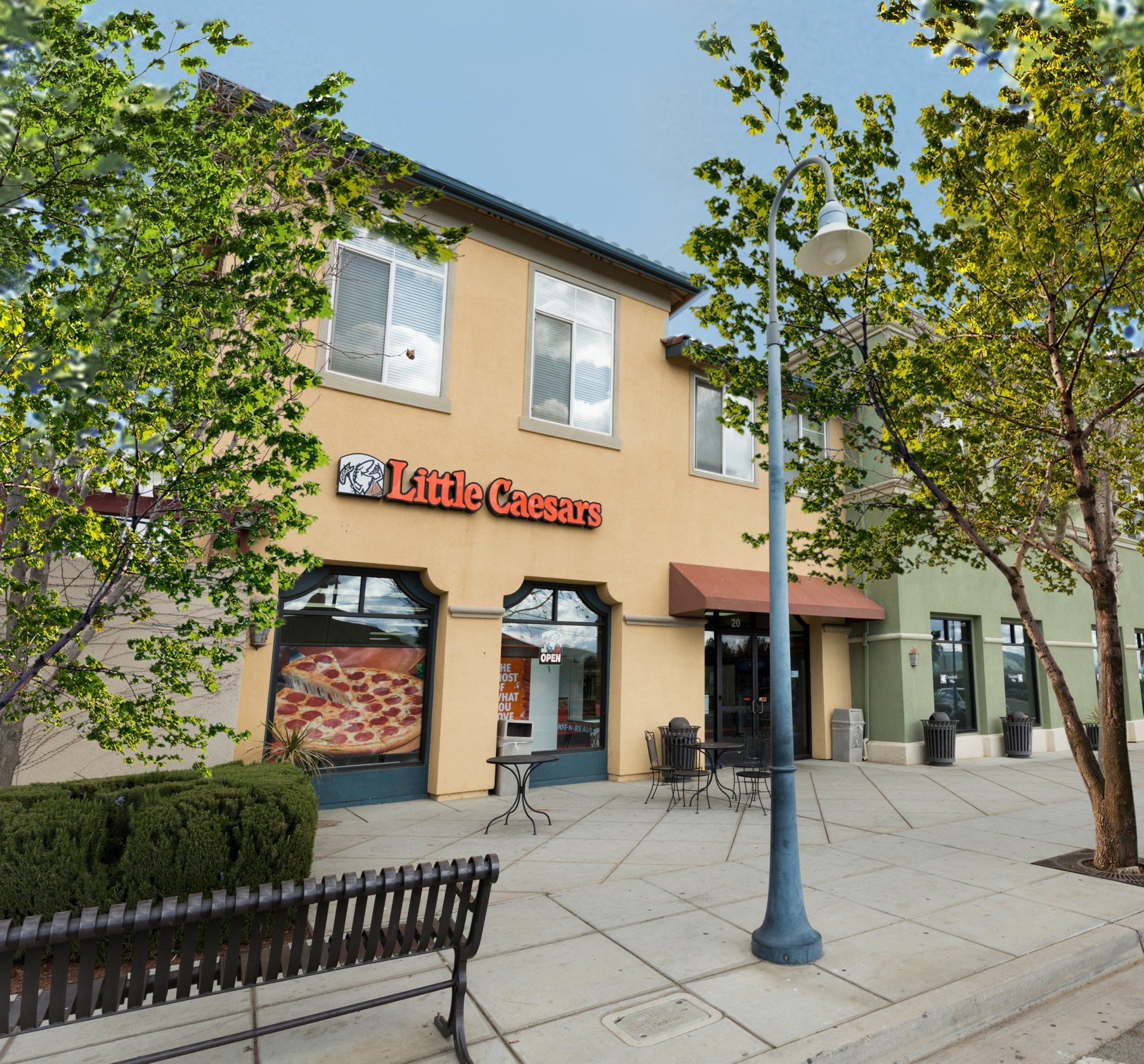 A little caesars restaurant with a bench in front of it