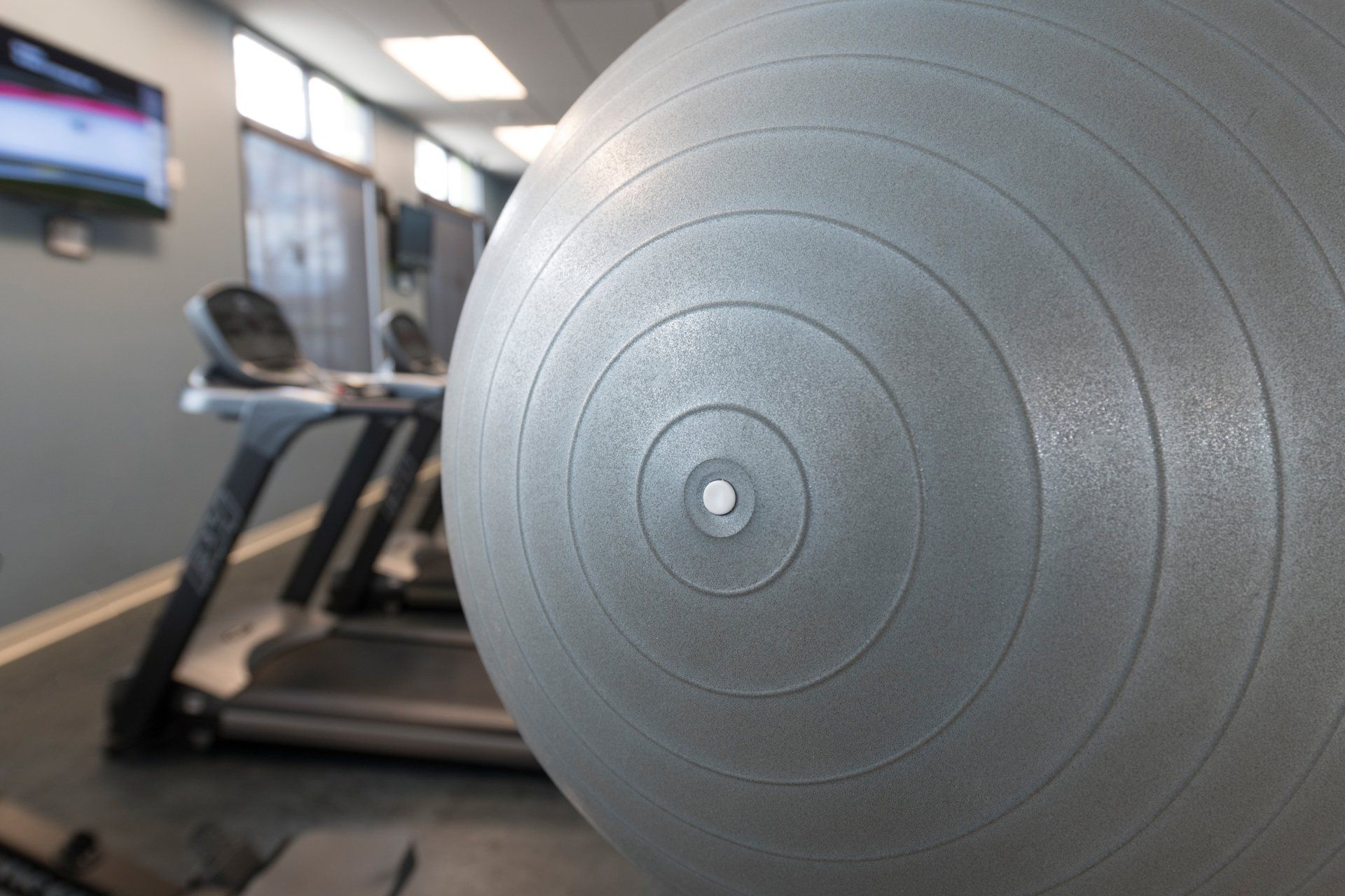 A gray exercise ball in a gym next to a treadmill