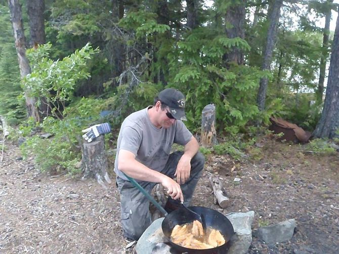A man is kneeling over a pot of food in the woods