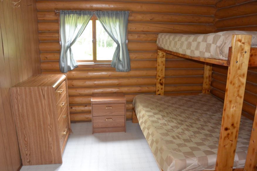 A bedroom in a log cabin with bunk beds , a dresser , and a window.