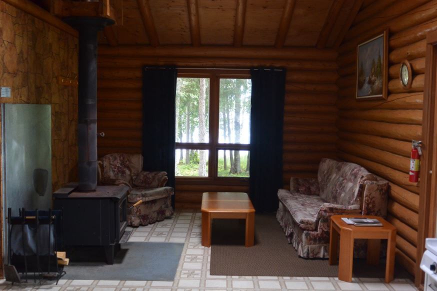 A living room in a log cabin with a couch and chairs