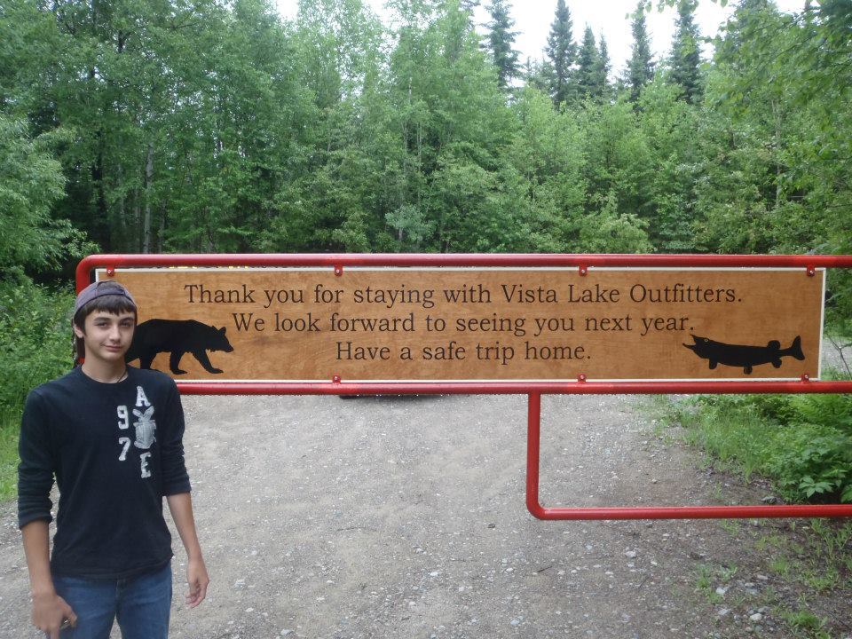 A young man stands in front of a sign that says thank you for staying with vista lake outfitters