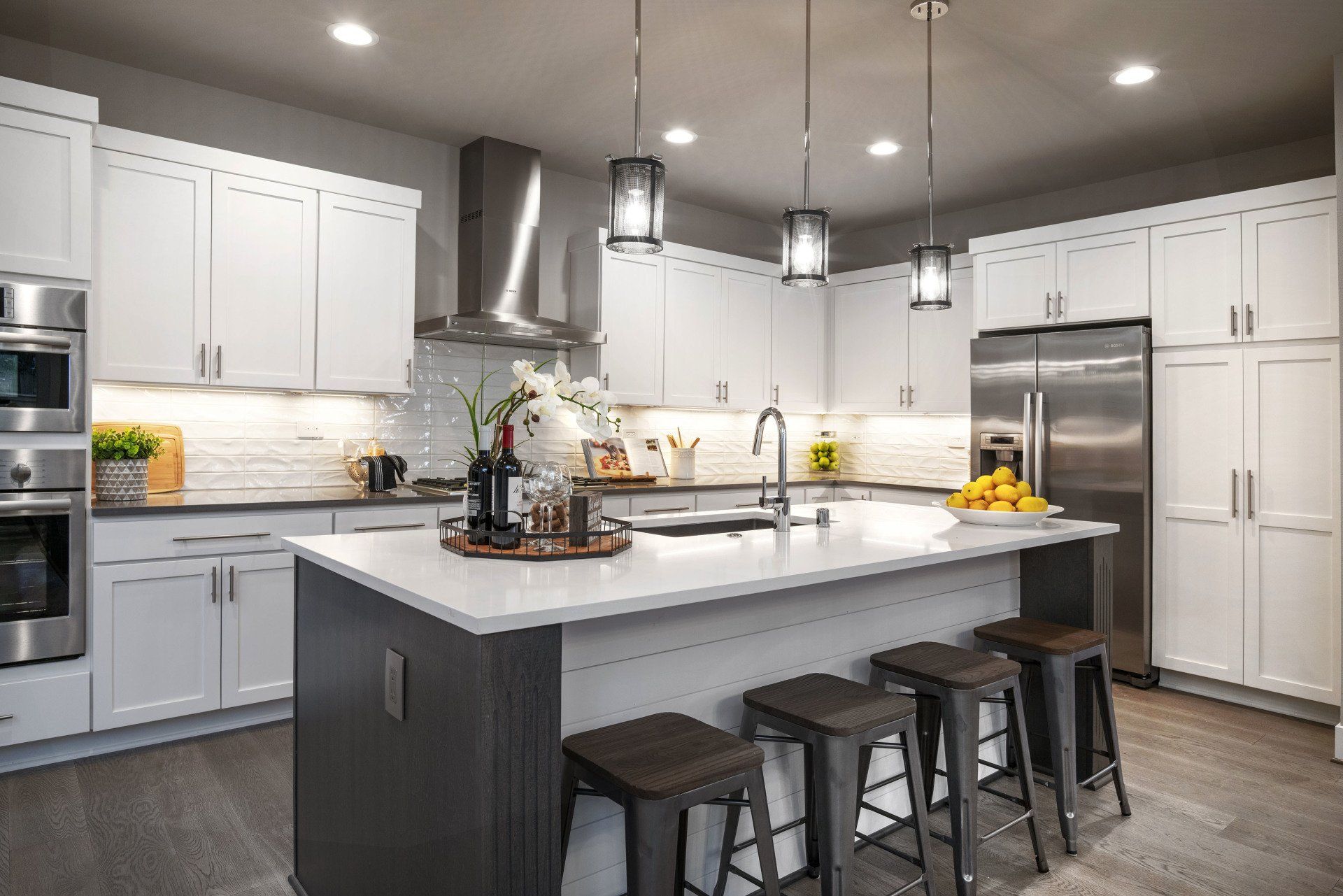 Modern white kitchen with central island, pendant lights, stainless steel appliances, and stools