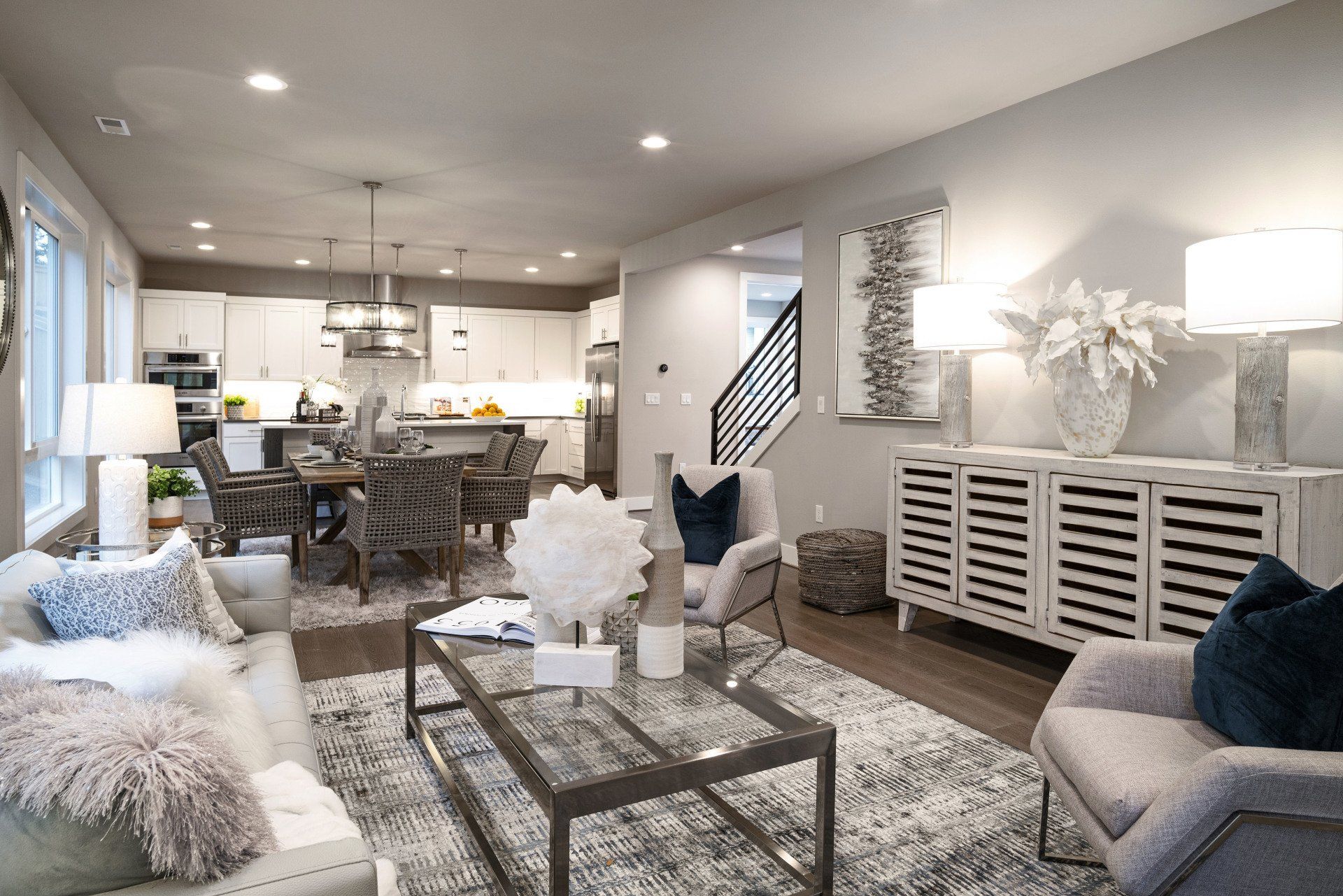 Bright modern open-plan living room with gray sofas, patterned rug, dining area, and kitchen in the background