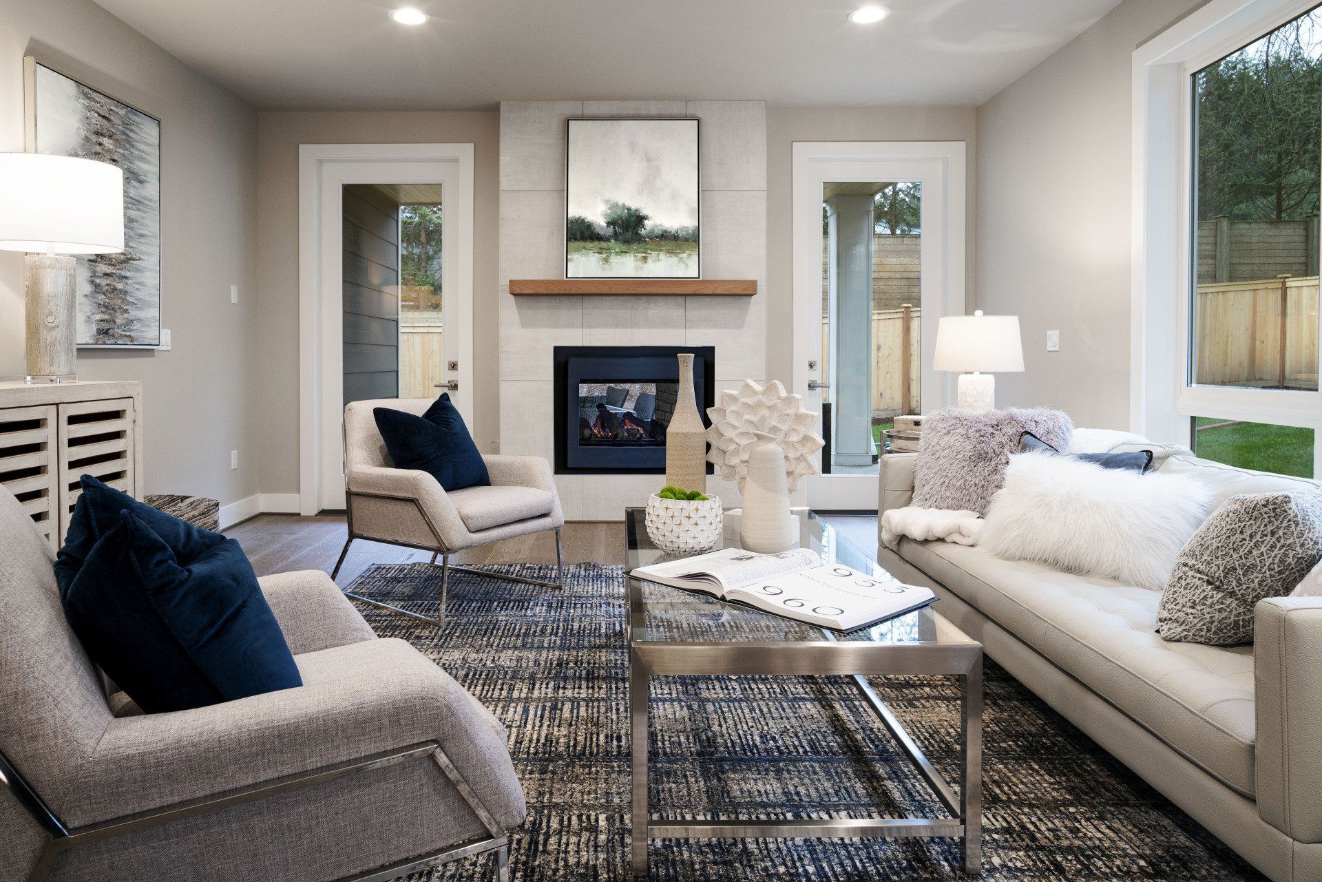 Bright modern living room with white sofas, gray chairs, a fireplace, and large windows