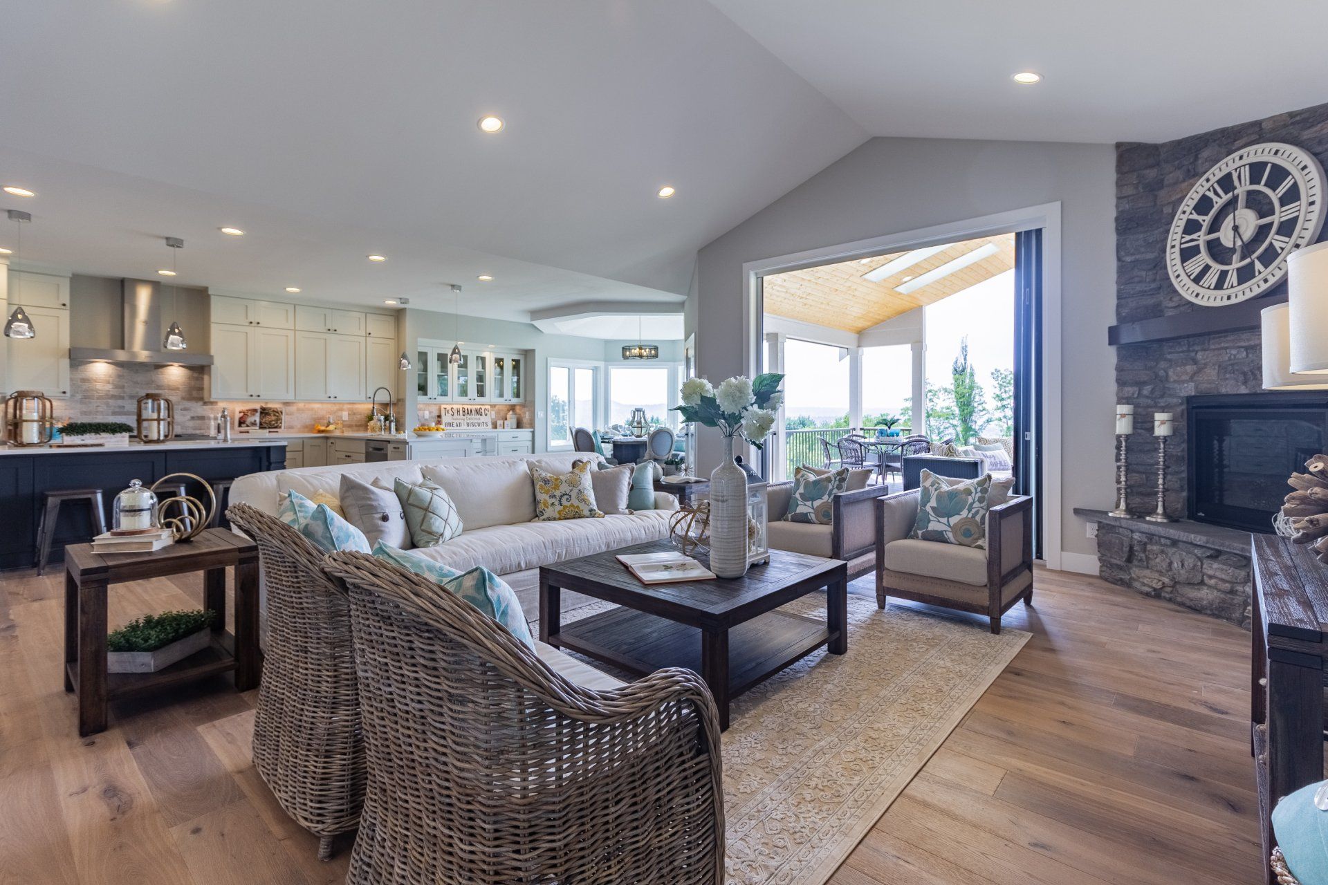 Open-plan living room with wicker seating, stone fireplace, and large windows