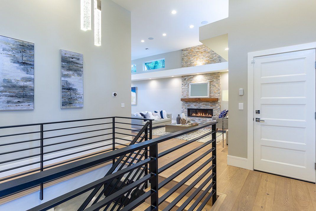 Modern home interior with open staircase, wood floors, white walls, and kitchen in the background
