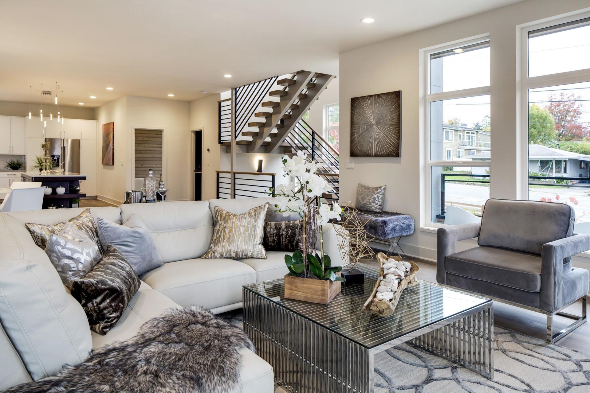 Modern living room with gray sectional, glass coffee table, armchair, and staircase by large windows