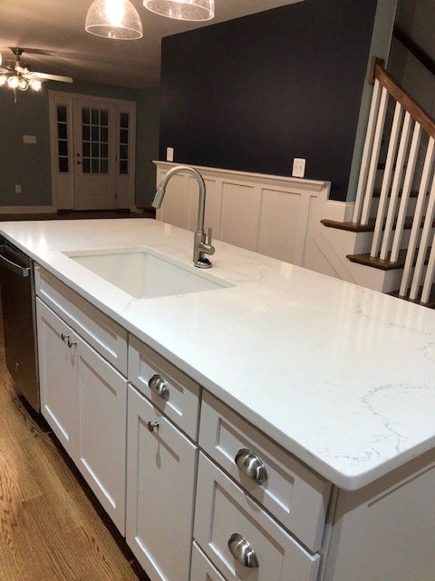 A kitchen with an island that has white cabinets and a sink