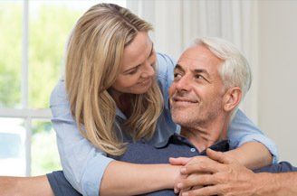 A woman is hugging an older man on a couch.