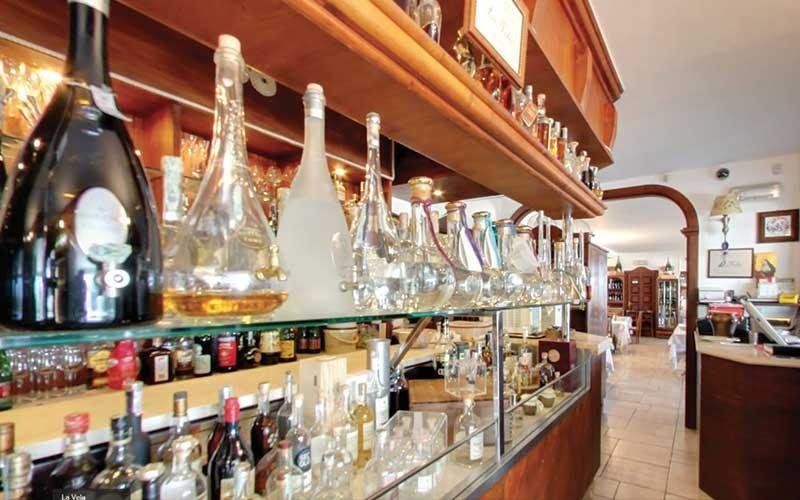 Bottiglie di liquore e bicchieri esposti su scaffali all'interno di un bar illuminato da una luce calda.