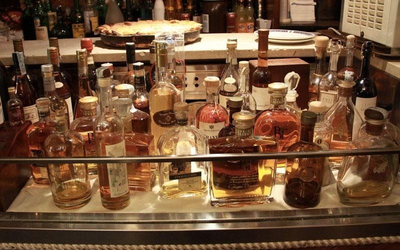 Diverse bottiglie di liquore su uno scaffale dietro un bancone di vetro.