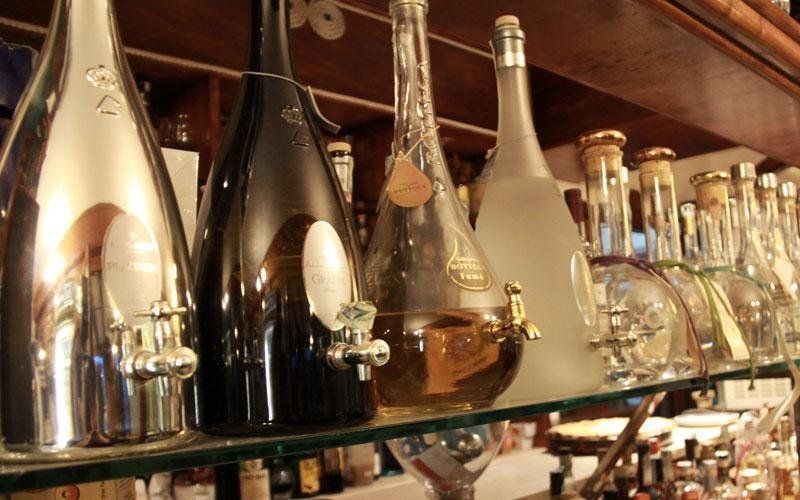 File di bottiglie di liquore su uno scaffale da bar, con decanter in metallo e bottiglie di vetro in una luce calda