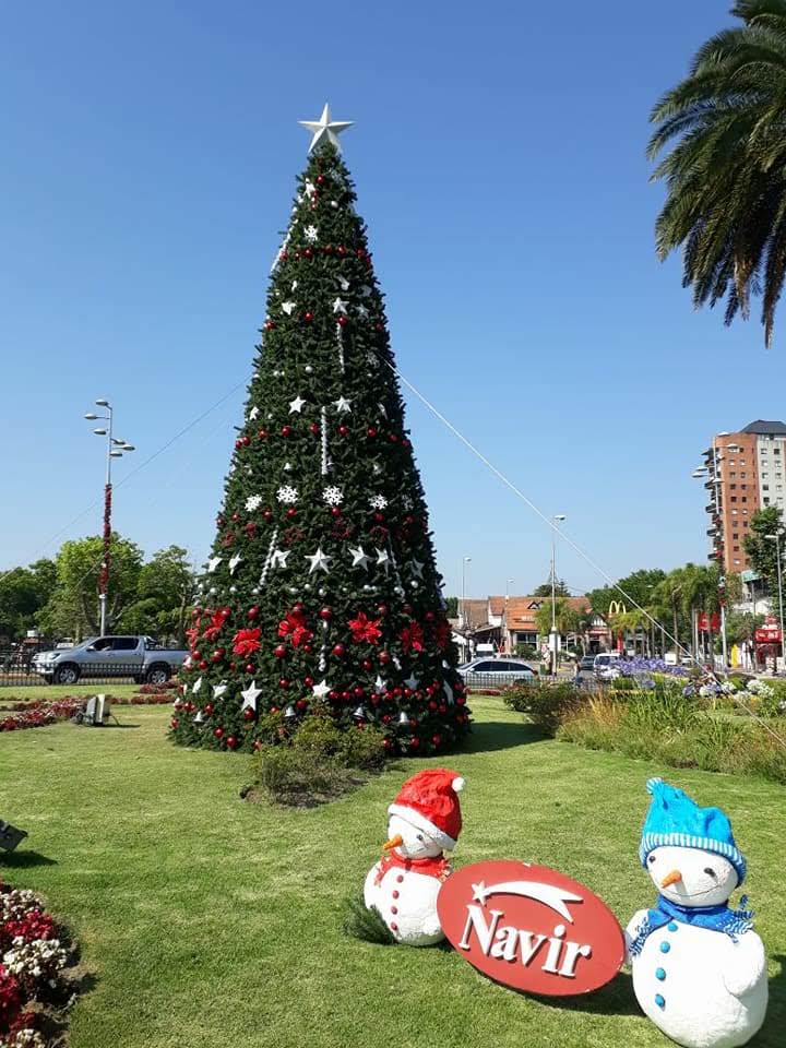 Árbol de Navidad decorado en un césped soleado con figuras de muñecos de nieve y un letrero de Navir delante.