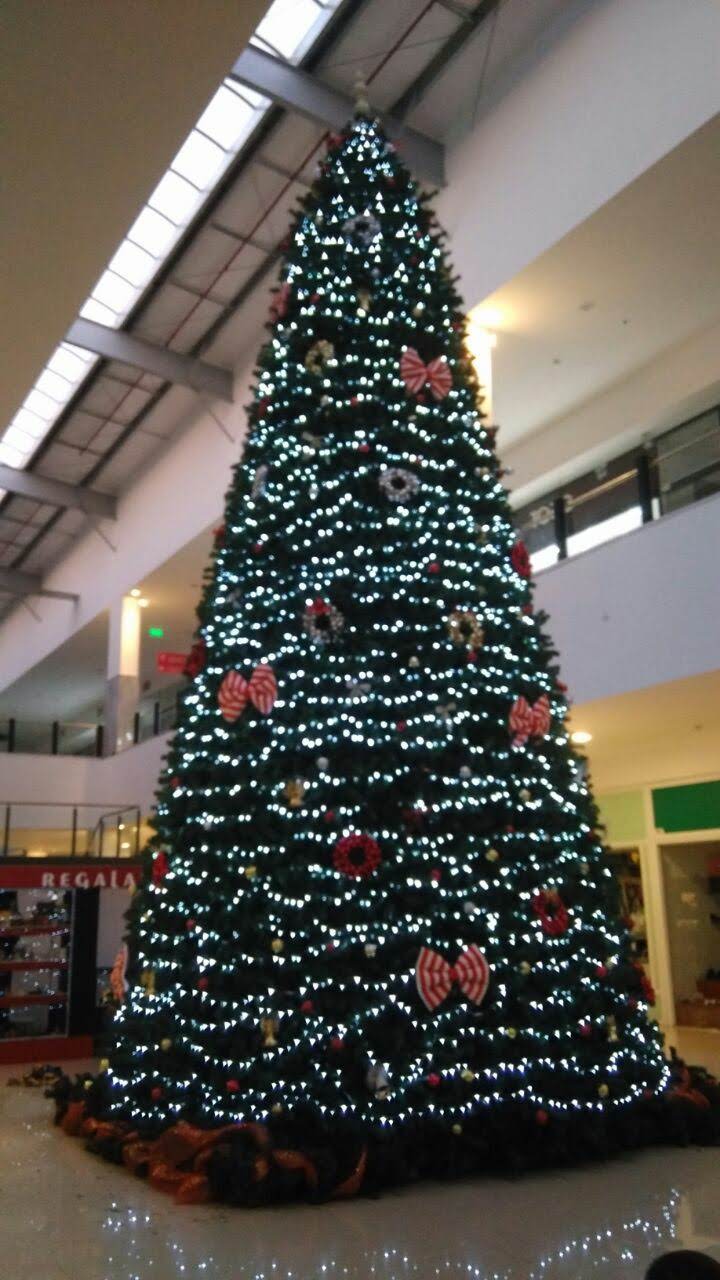 Árbol de Navidad alto y decorado con luces blancas y adornos rojos en el atrio de un centro comercial.