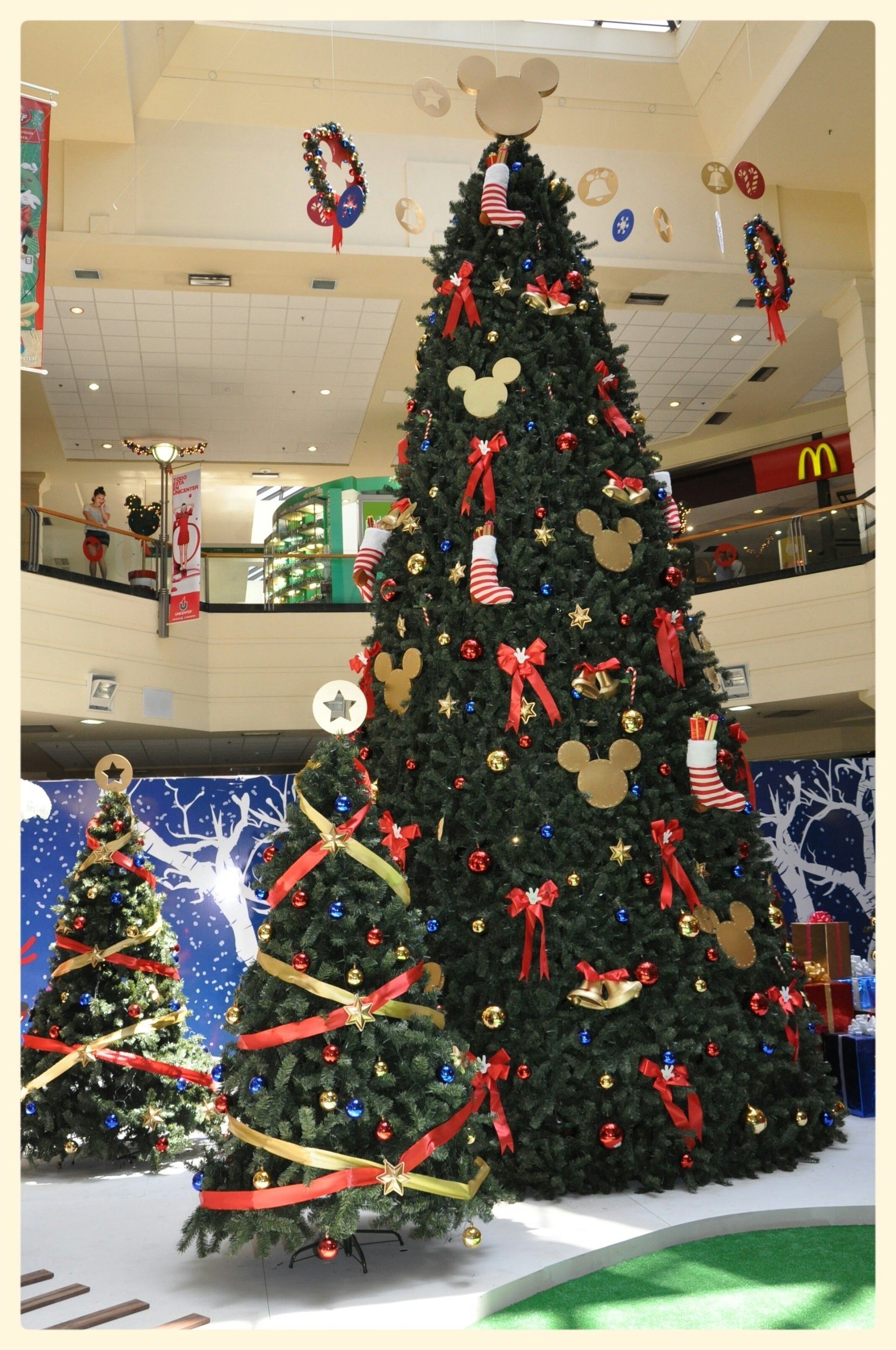 Árbol de Navidad decorado en un centro comercial con cintas rojas y adornos.