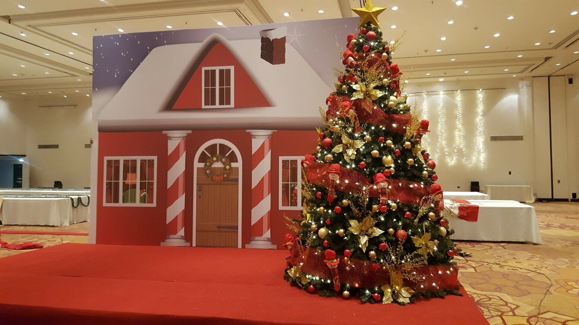 Decoración festiva de una casa roja junto a un árbol de Navidad decorado en el vestíbulo de un hotel.