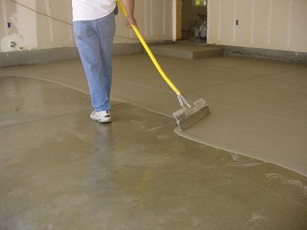 A person is using a yellow broom to spread concrete on the floor.