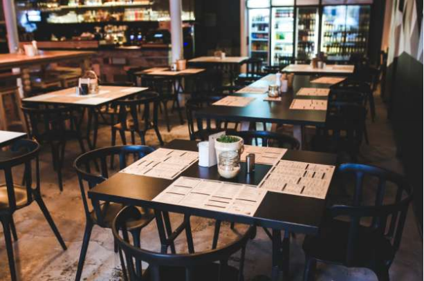 A restaurant with tables and chairs and a fridge in the background.
