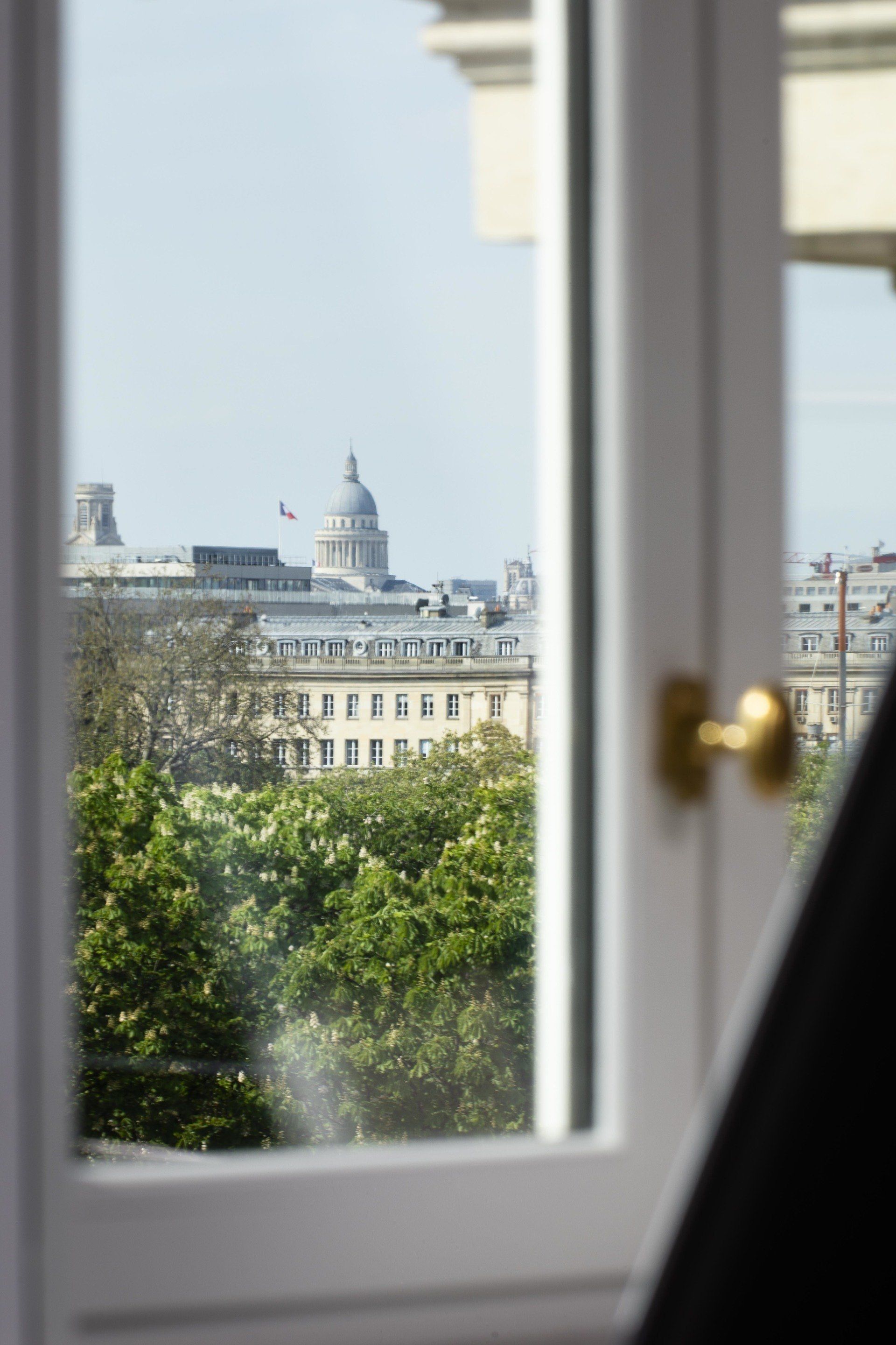 Une vue d'une ville depuis une fenêtre avec des arbres et des bâtiments en arrière-plan.