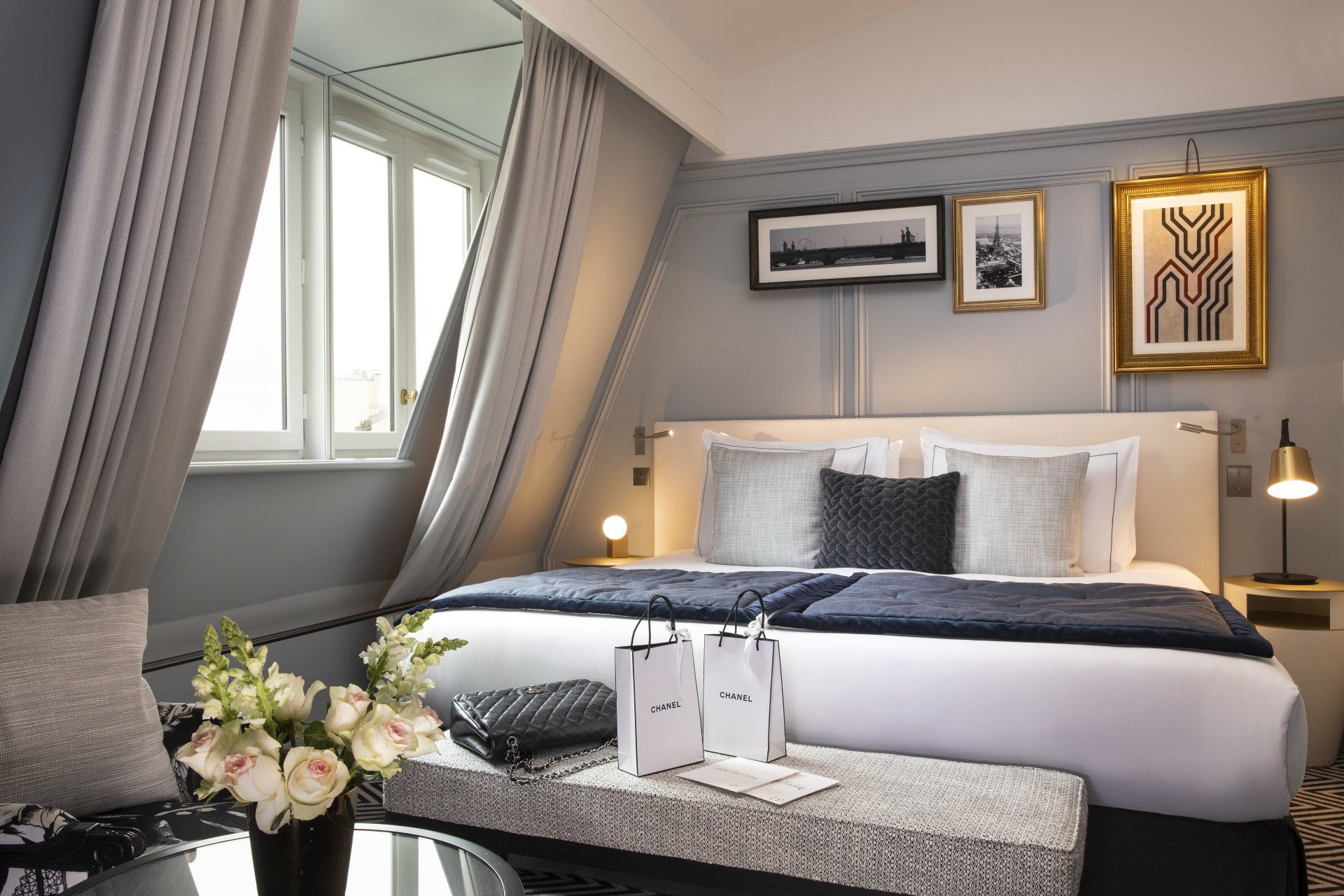 Une chambre d'hôtel avec deux lits, une table, un vase de fleurs et une fenêtre.